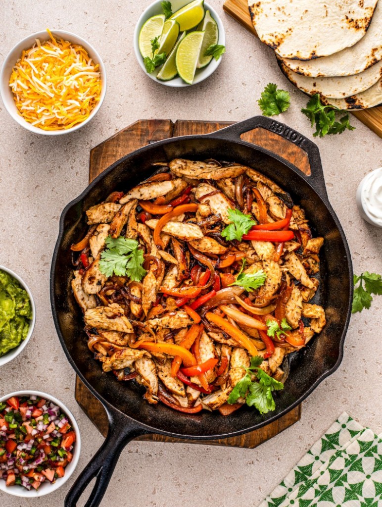 Chicken fajitas in a cast-iron skillet with tortillas and sides
